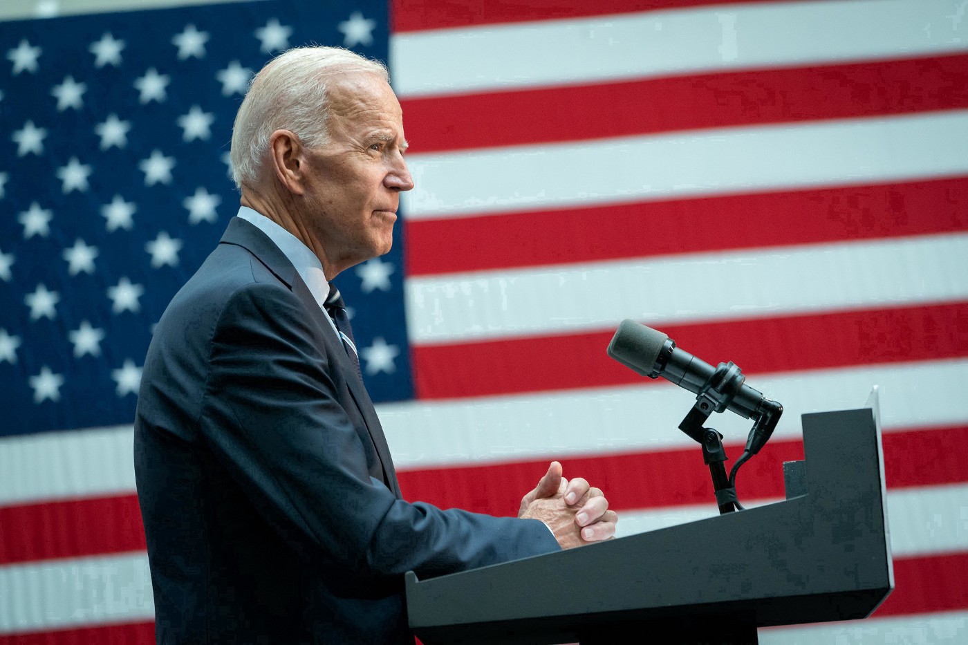 Joe Biden in profile standing at a podium in front of an American flag