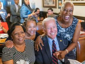 Joe at a diner with African American supporters. Three women are next to him and they are smiling at the camera and look happy.