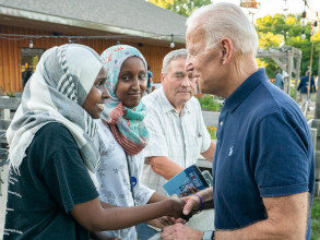 Joe shaking hands with a young woman wearing a hijab. They are both smiling and another woman in a hijab as well as an older man are standing nearby.
