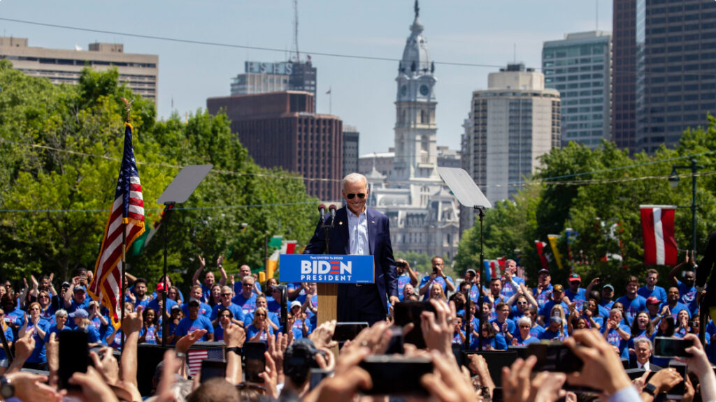 Joe Biden giving a speech outdoors in Philadelphia with a cheering crowd around him.